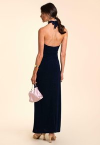 Robe maxi sans manches marine avec des détails froncés, assortie à un sac à main en satin rose clair et des chaussures à talons nude, sur un fond beige.