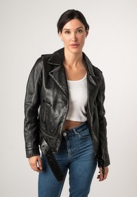 Giubbotto da moto in pelle nera con design aderente, rever a punta, cerniere e vita con cintura, abbinato a un top corto bianco e jeans blu.