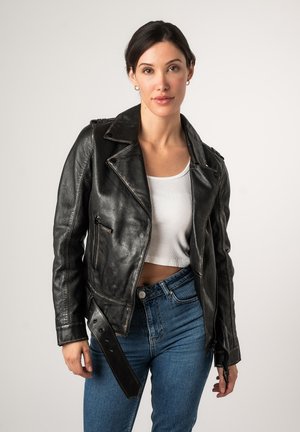 Veste en cuir noir de moto avec un design ajusté, des revers crantés, des fermetures éclair et une taille ceinturée, associée à un top court blanc et un jean bleu.