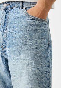 Ljusblå denimjeans med en präglad textdesign i olika typsnitt, femfickorsdesign och en normal passform.