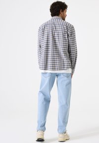 Gekleurde langslavige shirt in blauw en beige, gemaakt van stof met een zachte textuur. Draag met lichtblauwe jeans en crèmekleurige sneakers.