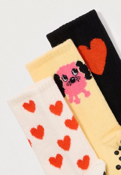 Kolm erksat sokki: valge punaste südametega, kollane roosa koerapildiga ja must suure punase südamega.