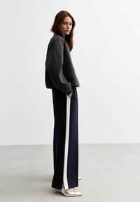 Donkergrijze, gestructureerde sweatshirt met een relaxed fit, gecombineerd met marineblauwe wijde broek met witte zijstrepen en zilveren puntige schoenen.