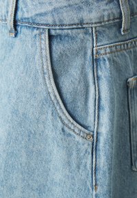 Lyseblå denimskjørt med en buet lomme med sølvfarget metallikk, solid søm og en lett falmet tekstur.