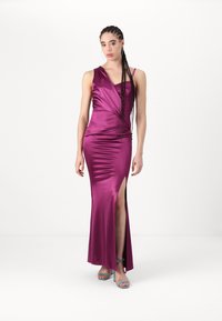 Rochie lungă, din satin magenta, cu un design pe o umăr și o fendere laterală. Prezintă o textură fină și detalii drapate. Asortată cu tocuri albastre.