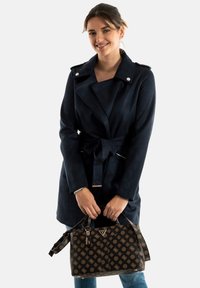 Trench-coat bleu marine, ceinturé, en daim doux avec un large col. Accompagné d'un sac à main à motif marron avec des accents en métal doré.