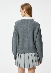 Grå stickad tröja med texturerad yta, med ribbat avslut och vida ärmar, tillsammans med en veckad grå kjol.