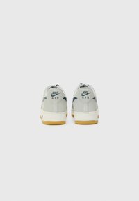 Nike Air sneakers with a light grey suede upper, navy accents, and a gum rubber outsole. Features signature logo on the heel.