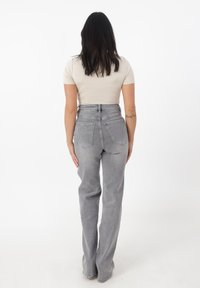 Jeans gris de talle alto con un corte relajado, que presentan bolsillos traseros y un acabado desgastado, combinados con una blusa ajustada de color beige claro.