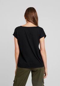 Camiseta de algodón negra con mangas cortas enrolladas y un escote amplio, combinada con pantalones cargo verdes oliva. Tejido texturizado, ajuste casual.
