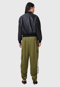Svart bomberjacka med slät textur, ribbade muddar och nederkant, i kombination med lösa olivgröna cargobyxor med sidofickor.