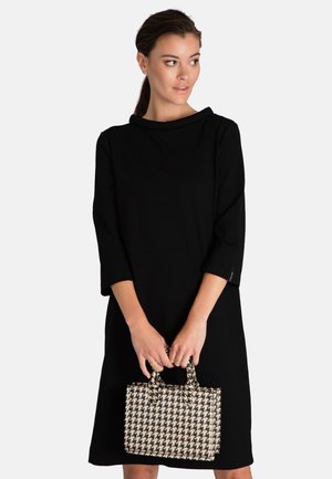 Zwarte lange mouw jurk met een col, gecombineerd met een kleine handtas in houndstooth-patroon met dubbele handvatten.