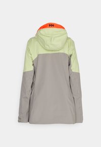 Wasserdichte Jacke mit einem grauen Körper, hellgrünen Ärmeln und einem orangen Akzent an der Kapuze sowie einem Logo im Nackenbereich.