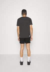 Svart treningst-skjorte med korte ermer, glatt tekstur og flate sømmer. Kombinert med svarte shorts og sokker, står på en ensfarget bakgrunn.