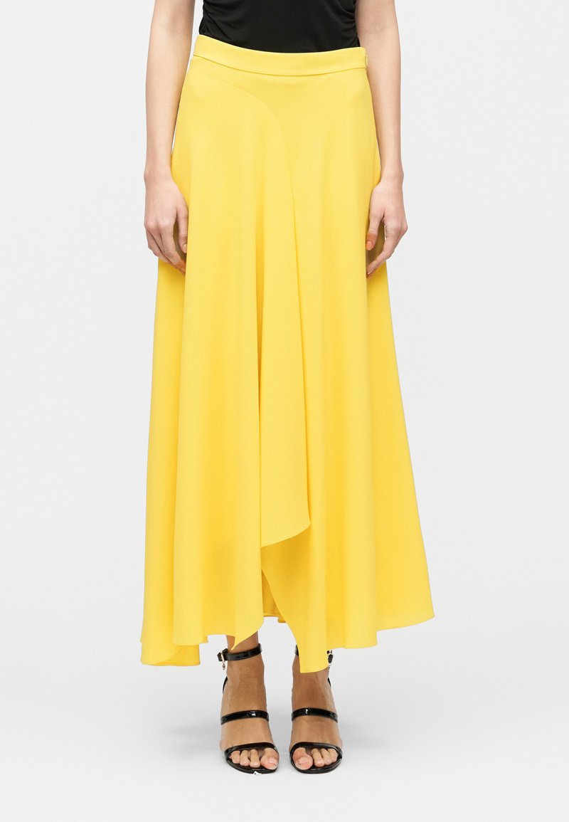 Jupe midi jaune fluide avec un ourlet asymétrique, confectionnée dans un tissu léger. Caractérisée par une taille ajustée et une texture lisse.