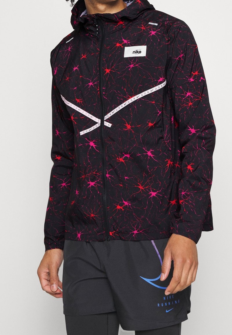 Zwarte jacket met een levendig roze en rood abstract patroon, voorzien van een rits aan de voorkant, een capuchon en reflecterende accenten.