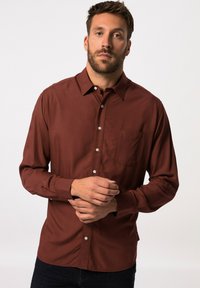 Camicia a maniche lunghe in tessuto rustico scuro, con colletto, chiusura a bottoni e tasca sul petto. Texture liscia, vestibilità sagomata, con polsini abbottonati.