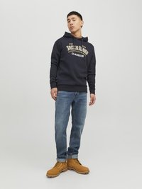 Felpa navy con logo, tasca frontale tipo kangaroo, abbinata a jeans azzurri e stivali alla caviglia beige con lacci e suole in gomma.