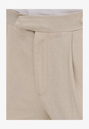 Jasnobeżowe lniane spodnie o plisowanym fasonie, gładkiej fakturze i dopasowanym pasku w talii. Brak widocznych kieszeni.