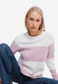 Maglione lavorato a maglia con larghe strisce orizzontali in rosa chiaro e bianco,collo rotondo e polsini a coste. Abbinato a jeans in denim blu.