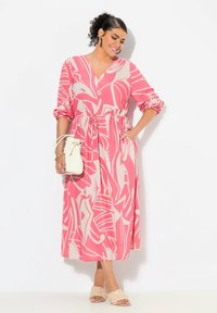 Rosa Maxikleid mit abstrakten beigen Mustern, V-Ausschnitt, gerafftem Taillenbund und langen Ärmeln. Kombiniert mit einer weißen Handtasche und gewebten beigen Mules.