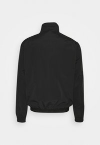 Czarna kurtka typu windbreaker z wysokim kołnierzem, elastycznymi mankietami i ściągaczem na dole z akcentem logo. Gładki, lekki materiał.