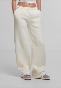Pantalons de survêtement de couleur crème avec une taille élastique, des poches latérales et des accents de motif subtils. Fabriqués en matériau doux et épais.