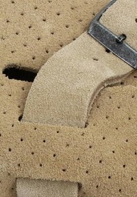 Sandale en daim avec un design perforé, de couleur beige, bride réglable avec une boucle métallique et une surface texturée.
