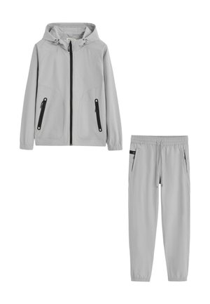 Veste à capuche gris clair avec poches zippées noires et pantalon assorti à taille élastique avec poches latérales et cordon.