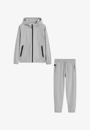 Veste à capuche gris clair avec poches zippées noires et pantalon assorti à taille élastique avec poches latérales et cordon.