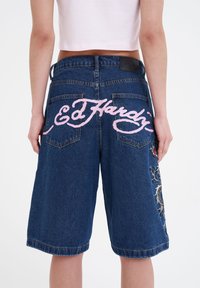Pantalones cortos de mezclilla con un ajuste holgado, color azul oscuro, logo bordado en rosa "Ed Hardy" en la parte trasera y un intrincado diseño de dragón.