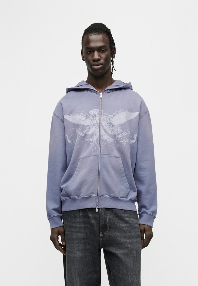 Μωβ φούτερ με φερμουάρ, διακοσμημένο με γραφικό αετού και κείμενο μπροστά. Διαθέτει κουκούλα, μπροστινές τσέπες και ριμπ μανσέτες. Απαλή υφή υφάσματος.