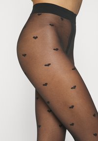 Collant neri trasparenti con motivo a cuori neri, caratterizzati da una texture liscia e una vita larga e solida.