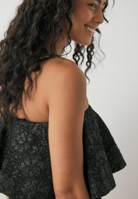 Čierny top s kvetinovým výšivkom bez ramienok, textúrovaný materiál a rozšírený strih. Obsahuje zberaný pás pre dobré prispôsobenie.