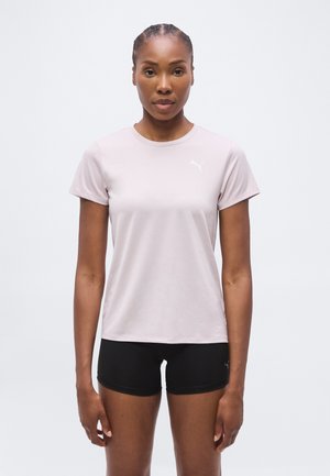 Femme portant un t-shirt Puma rose clair et un short de sport noir, debout devant un fond clair uni, face à l’avant.