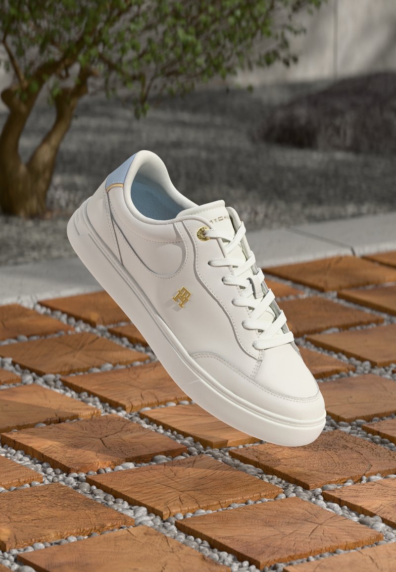 Hvit lær sneaker med en glatt tekstur, gullakenter og en lyseblå innersåle. Har et klassisk snøring-design og polstret tunge.