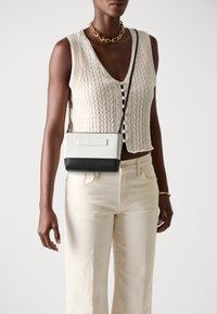 Small rectangular handbag in white and black leather, featuring a textured design and a detachable shoulder strap.