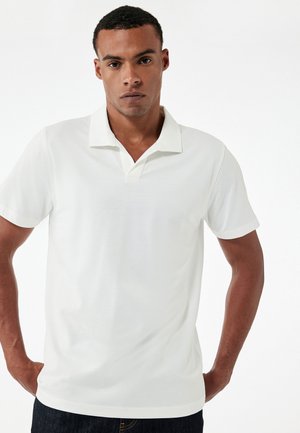 Polo shirt blanc avec un col, des manches courtes et un tissu lisse et texturé. Présente un design classique adapté à une tenue décontractée.