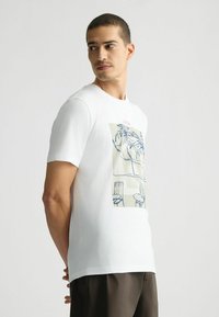 Tricou alb din bumbac cu un imprimeu grafic care prezintă desene cu linii albastre ale palmierilor și scaunelor pe un fundal deschis. Mâneci scurte.