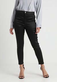 Svarta fusk läderbyxor med hög midja, metallknappstängning och slim fit. Matchas med en ljusgrå blus och svarta klackar med remmar.