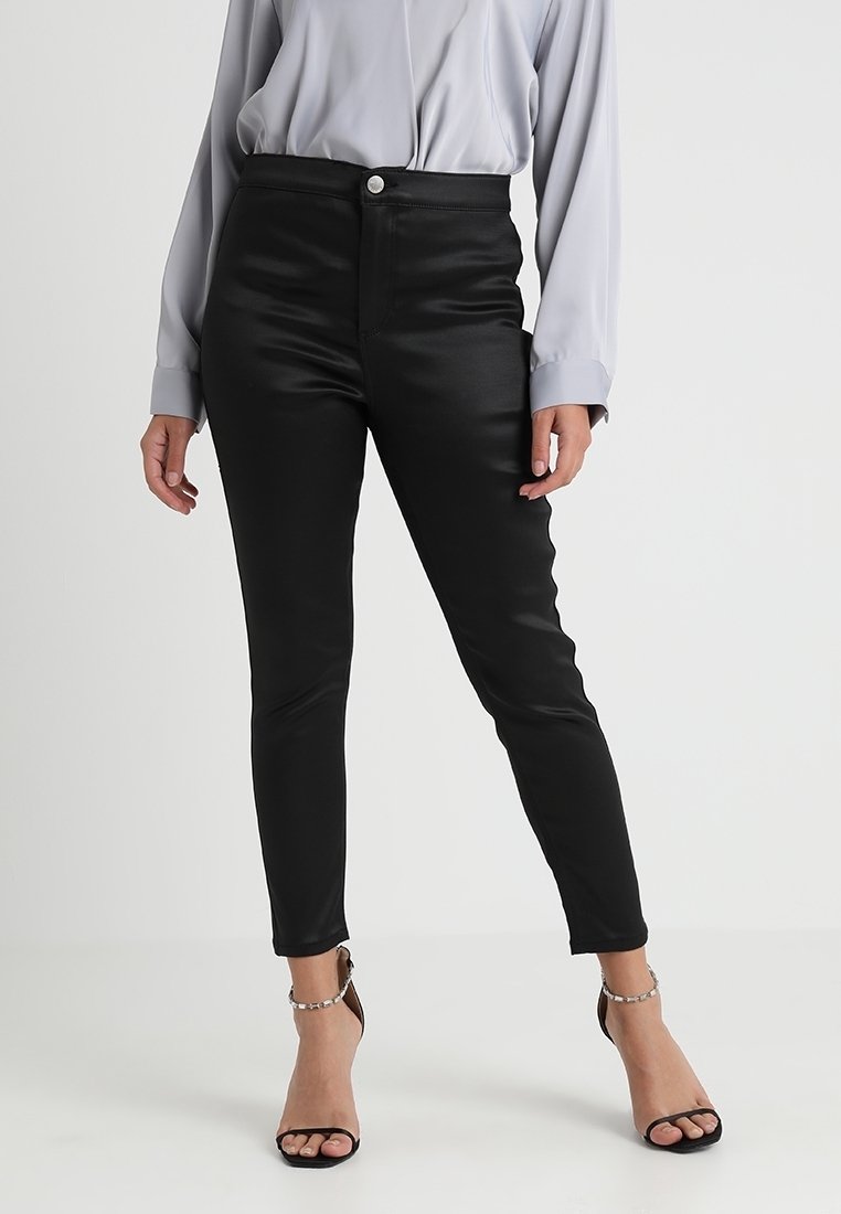 Svarta fusk läderbyxor med hög midja, metallknappstängning och slim fit. Matchas med en ljusgrå blus och svarta klackar med remmar.