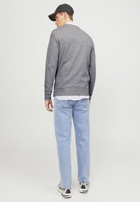 Gray sweatshirt with a crew neck, long sleeves, and ribbed cuffs, worn over a white and blue striped shirt, paired with light blue jeans.