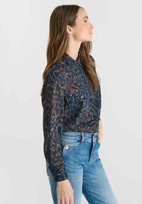 Button-up shirt in dark blue with a patterned design in brown and orange hues. Features a collar, long sleeves, and two front pockets.