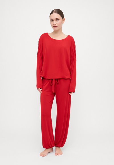 Red loungewear set featuring a loose-fit long-sleeve top with wide neckline and matching drawstring pants with tapered ankles. Soft fabric.