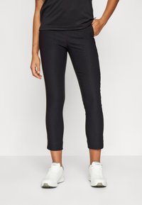 Pantaloni capri neri attillati con una texture liscia e vita media. Indossati con scarpe da ginnastica bianche. Dettagli di cucitura sottili sulla parte frontale.