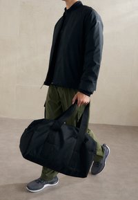 Borsa duffle nera con due manici lunghi, realizzata in un materiale resistente, dotata di un ampio interno e di una texture liscia.