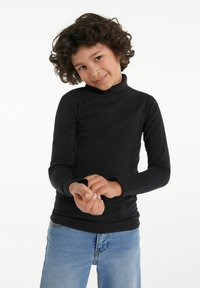 Schwarzes langärmliges Rollkragen-Shirt aus weichem Stoff, taillierte Passform und gerippte Textur, kombiniert mit hellblauen Jeans.