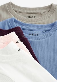 Pile de hauts à col rond côtelés en beige, bleu clair, violet foncé, rose et blanc avec des étiquettes de marque NEXT visibles à l'intérieur des cols.