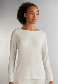 Světle šedý top s dlouhým rukávem, ribovací textura, široký výstřih a spadlé ramenní švy. Měkká tkanina se subtílními vertikálními pruhy.