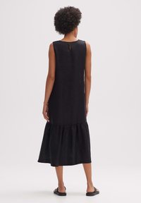 Svart linneklänning med ärmlös design, med detaljer som nyckelhål i ryggen och en lagerpuffig nederkant. Slät textur, ankel-lång klipp.